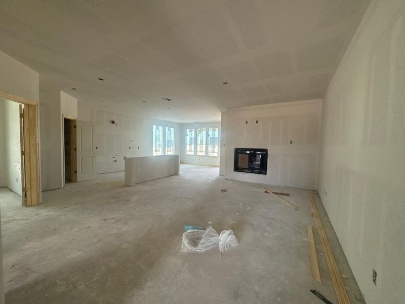 Spacious interior with drywall completed throughout, featuring a prominent built-in fireplace with a black glass insert Spacious interior with drywall completed throughout, featuring a prominent built-in fireplace with a black glass insert