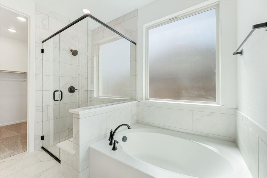 Bathroom with soaking tub, glass-enclosed shower, white marble tile, and frosted window near walk-in closet