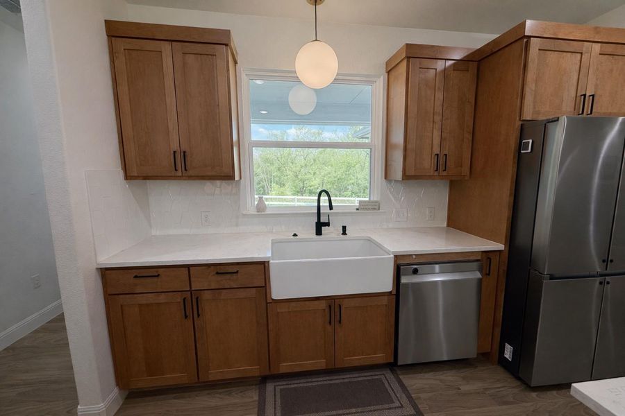 Kitchen featuring appliances with stainless steel finishes, brown cabinetry, decorative light fixtures, and decorative backsplash Kitchen featuring appliances with stainless steel finishes, brown cabinetry, decorative light fixtures, and decorative backsplash