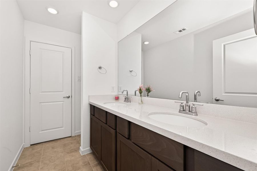 Upstairs bathroom vanity area featuring dual sinks, ample counter space, and a large mirror. Functional layout with dark cabinetry, neutral finishes, and tile flooring designed to comfortably serve the upstairs bedrooms and shared living spaces.