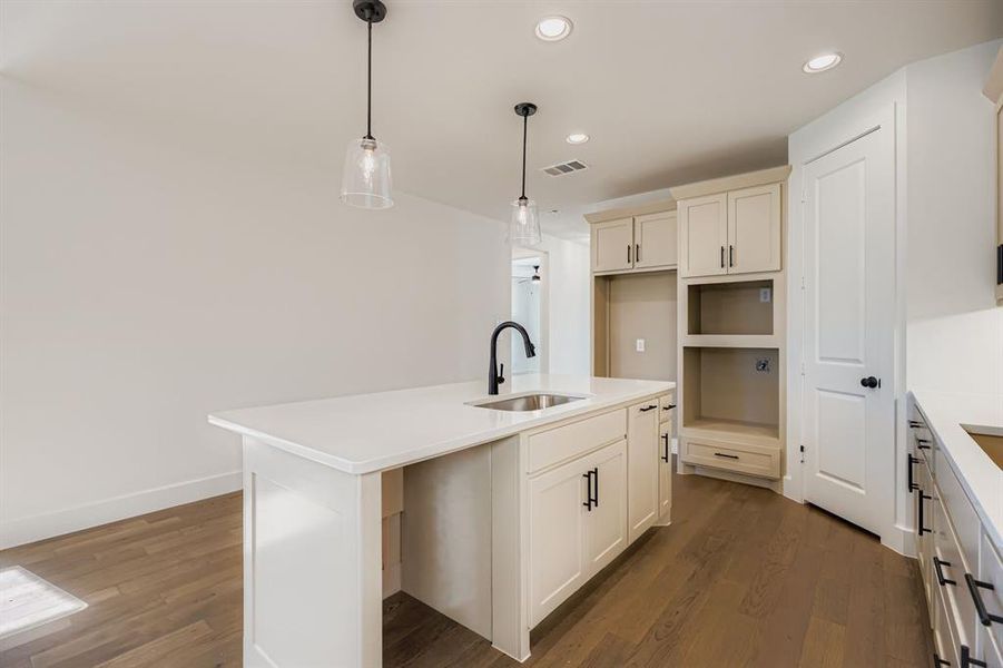 Kitchen with a center island with sink, dark wood-style floors, hanging light fixtures, recessed lighting, and light stone countertops Kitchen with a center island with sink, dark wood-style floors, hanging light fixtures, recessed lighting, and light stone countertops