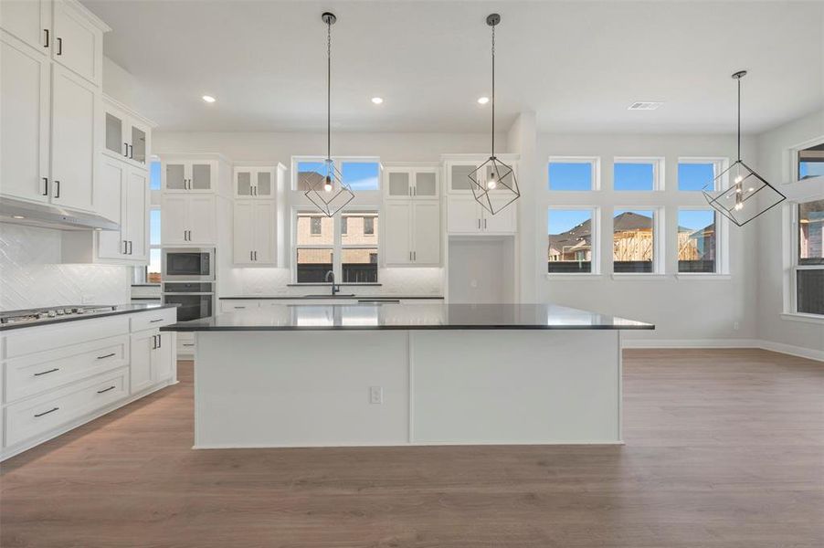 Kitchen with white cabinetry, a large island, light wood-type flooring, and tasteful backsplash