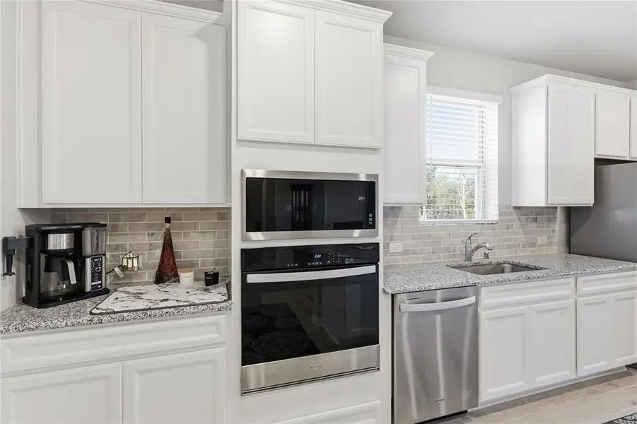 Kitchen featuring white shaker-style cabinetry, stainless steel appliances, granite countertops, and a subway tile backsplash