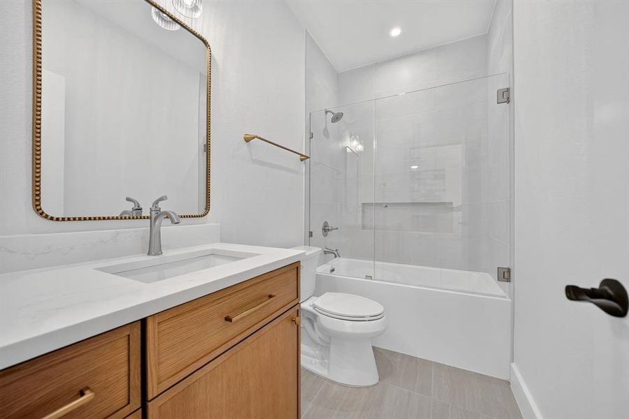 Bathroom featuring a wood-finish vanity with a white countertop and integrated sink, framed mirror, and a tub-shower combination with a clear glass enclosure and tiled surround