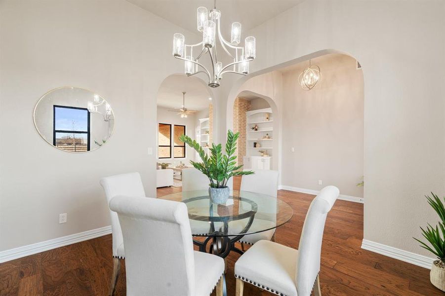 Dining space with ceiling fan with notable chandelier, built in shelves, and wood-type flooring