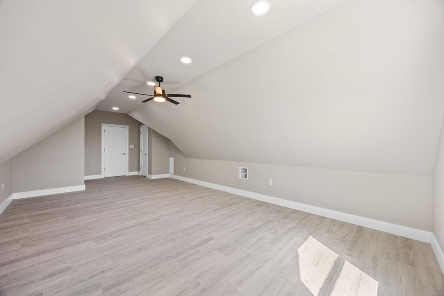 Bonus room featuring baseboards, recessed lighting, light wood-style flooring, visible vents, and lofted ceiling Bonus room featuring baseboards, recessed lighting, light wood-style flooring, visible vents, and lofted ceiling