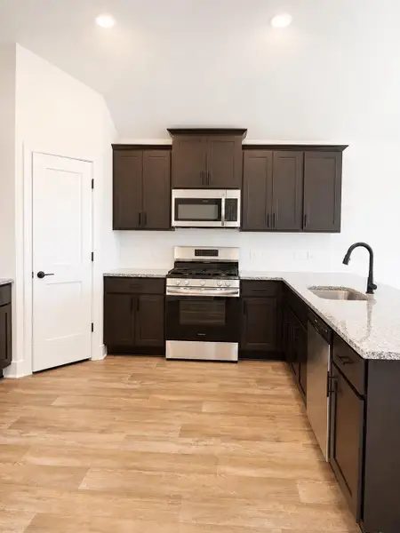 Open-concept kitchen view showcasing granite countertops, modern dark cabinetry, stainless steel appliances, recessed lighting, and a large island with plenty of prep and seating space.