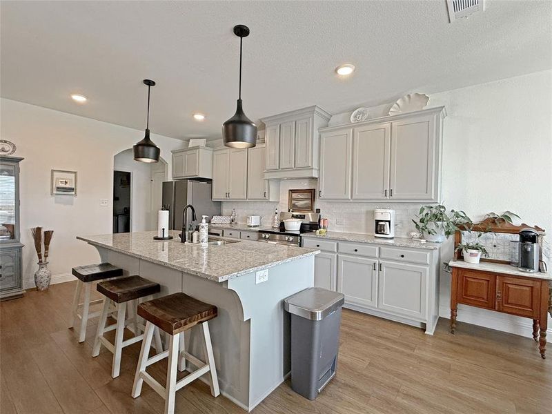 Kitchen featuring backsplash, a breakfast bar, hanging light fixtures, a kitchen island with sink, and recessed lighting Kitchen featuring backsplash, a breakfast bar, hanging light fixtures, a kitchen island with sink, and recessed lighting