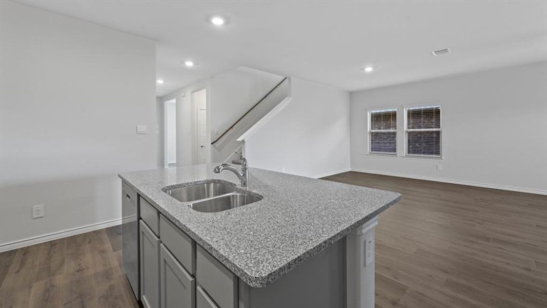Kitchen featuring gray cabinets, dark wood finished floors, an island with sink, light stone countertops, and open floor plan Kitchen featuring gray cabinets, dark wood finished floors, an island with sink, light stone countertops, and open floor plan