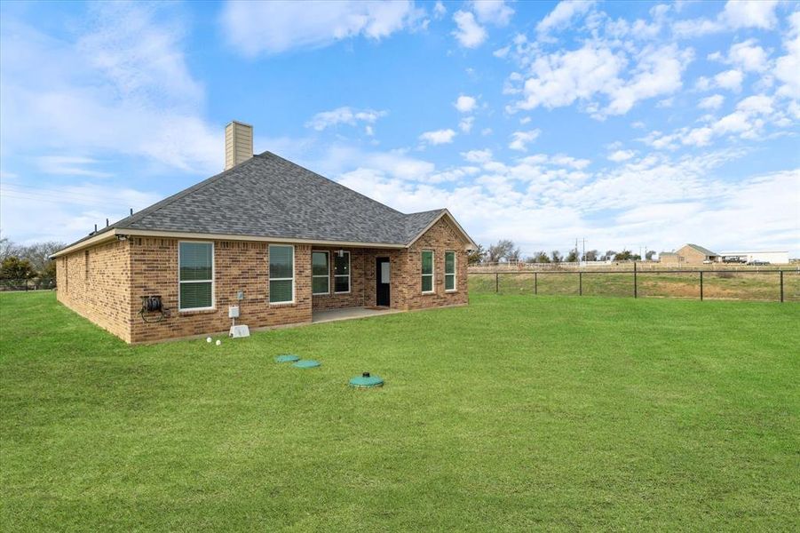 Back of house featuring brick siding, a yard, a chimney, a shingled roof, and fence