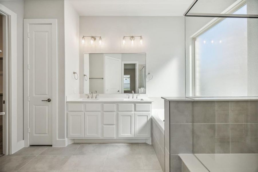 Bathroom featuring tile patterned flooring, vanity, and a relaxing tiled tub