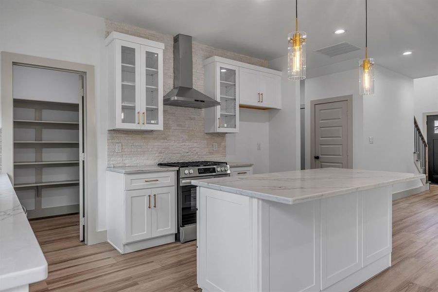 Kitchen with white cabinets, wall chimney range hood, pendant lighting, stainless steel range with gas stovetop, and backsplash Kitchen with white cabinets, wall chimney range hood, pendant lighting, stainless steel range with gas stovetop, and backsplash