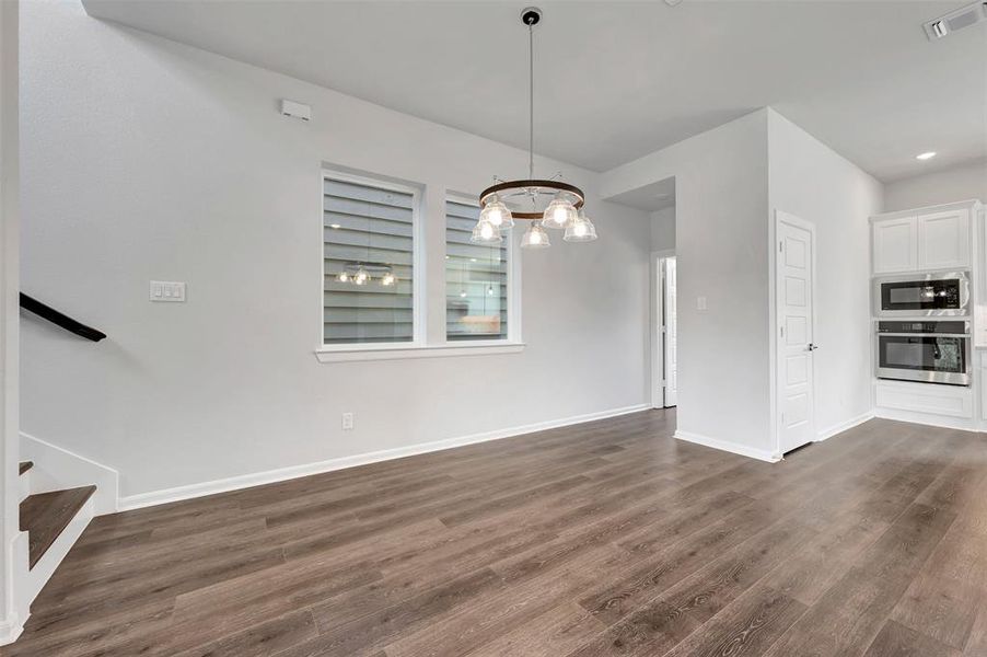 Spacious room featuring wood-finish flooring, white baseboards, and a contemporary chandelier