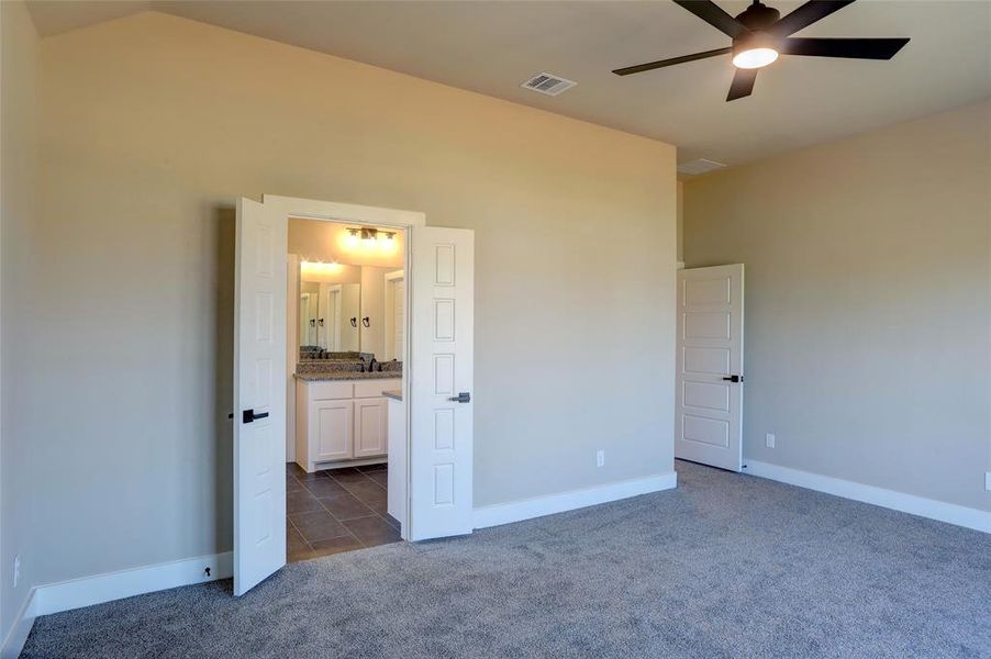 Unfurnished bedroom with dark carpet, ensuite bathroom, ceiling fan, and dark tile patterned flooring Unfurnished bedroom with dark carpet, ensuite bathroom, ceiling fan, and dark tile patterned flooring