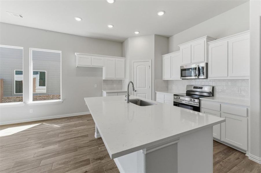 Kitchen featuring white cabinets, stainless steel appliances, light wood-style flooring, an island with sink, and recessed lighting