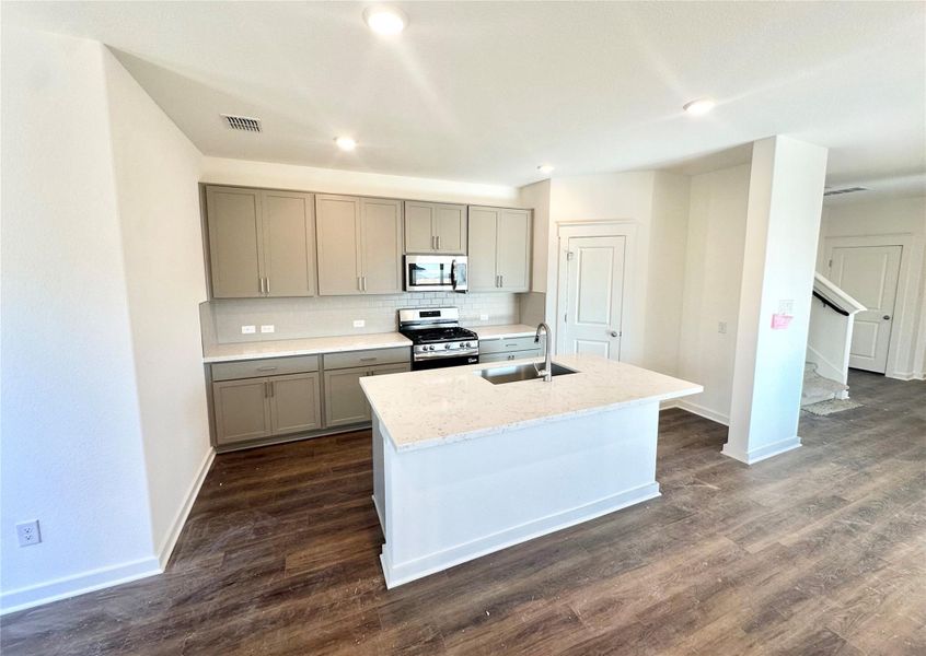 Kitchen with appliances with stainless steel finishes, an island with sink, light stone countertops, gray cabinets, and dark wood finished floors
