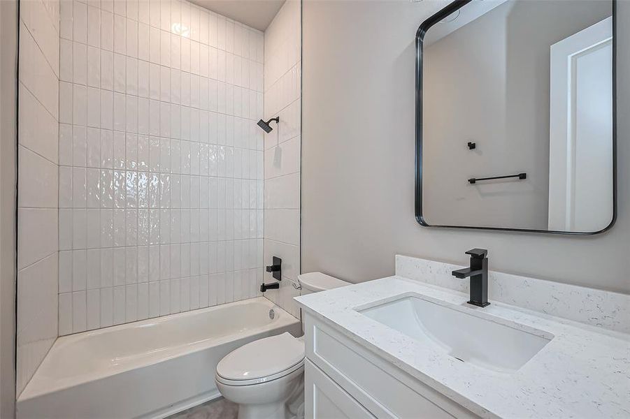 Discover modern elegance in this bathroom, featuring a white tiled shower-tub combo, sleek black fixtures, and a crisp white countertop with a rectangular sink. A large mirror and light walls enhance the bright, open ambiance.