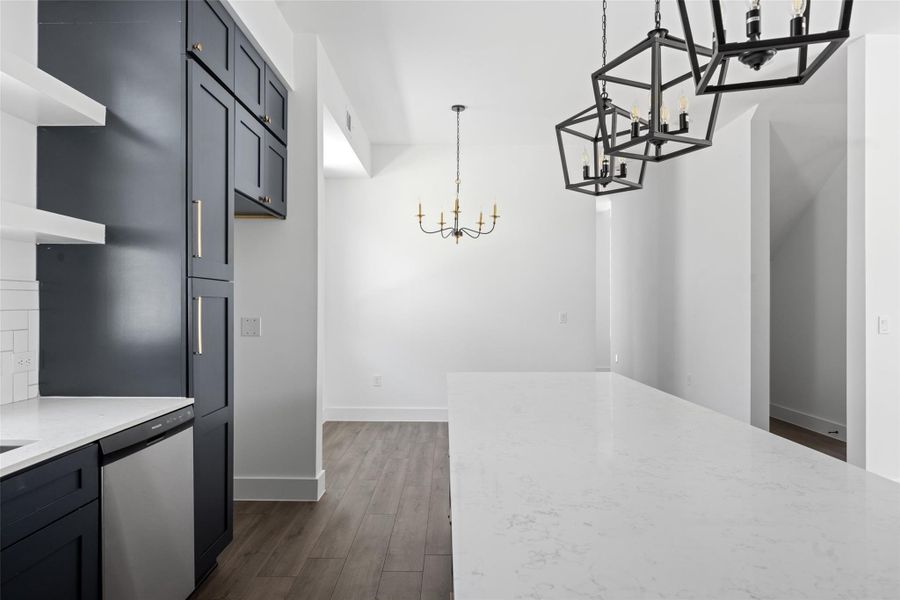 Kitchen with dark wood finished floors, stainless steel dishwasher, light stone counters, a chandelier, and decorative light fixtures Kitchen with dark wood finished floors, stainless steel dishwasher, light stone counters, a chandelier, and decorative light fixtures