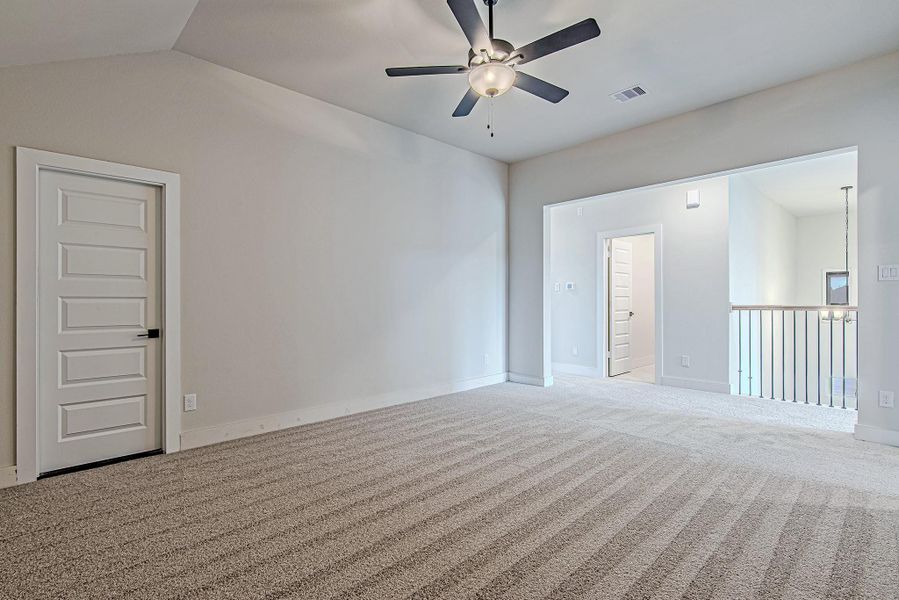 An upstairs game room or media flex space with vaulted ceilings, fresh neutral carpet, and convenient access to adjoining bedrooms and attic storage.