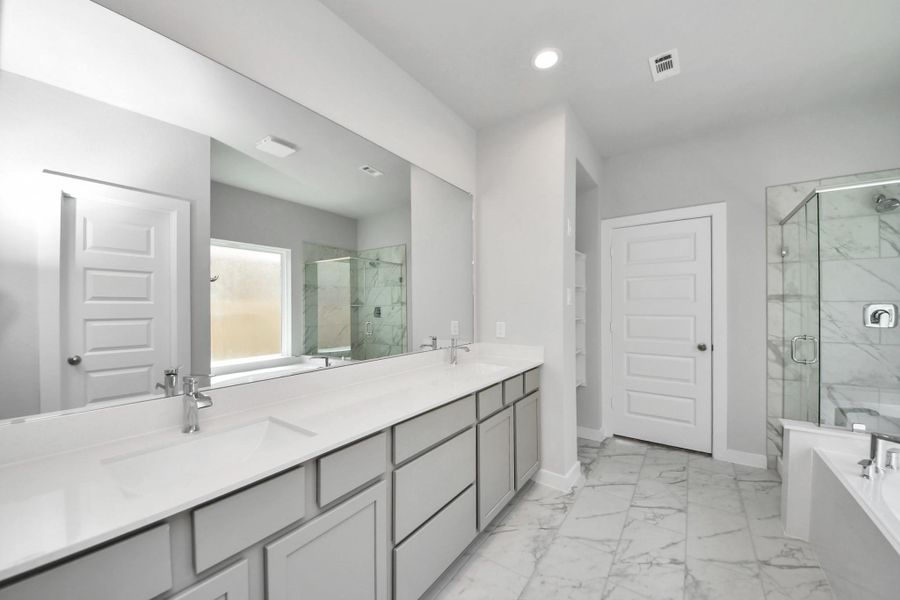 Escape to a spa-like oasis in this primary bathroom. Enjoy a walk-in shower with tile surround, a separate garden tub with custom detailing, and an elegant vanity featuring light countertops, modern hardware, and beautiful recessed lights. Experience luxury and relaxation in every detail. Sample photo of completed home with similar floor plan. Actual colors and selections may vary.