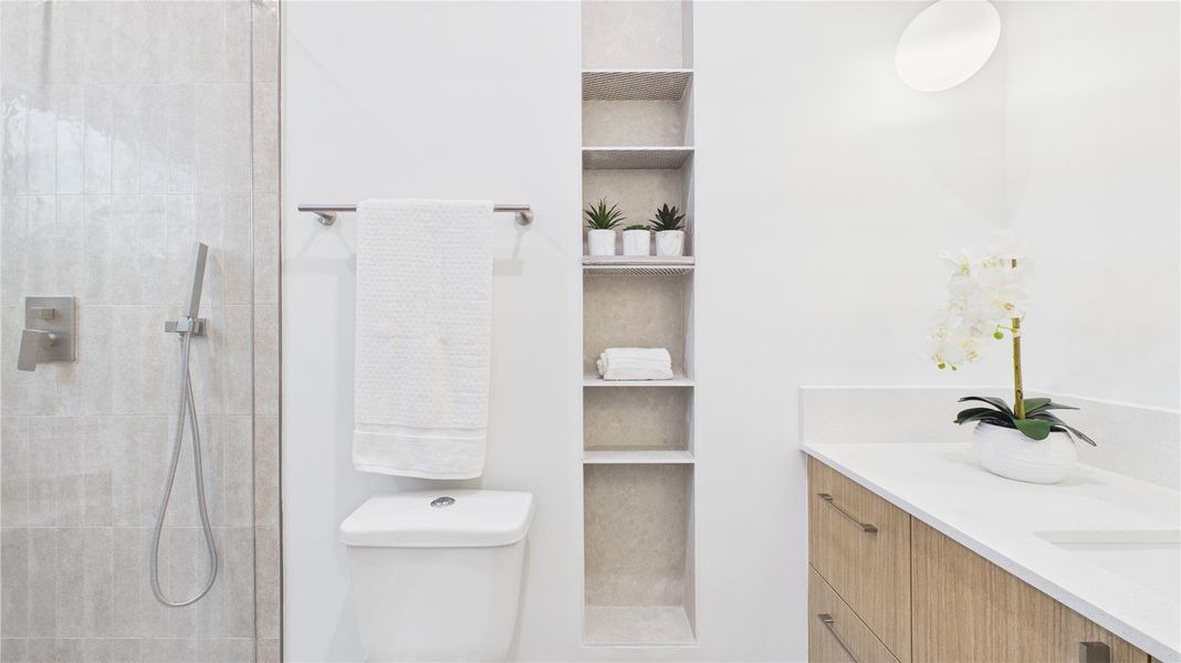 This bathroom features a sleek design with a glass shower, modern fixtures, built-in shelving, and a wooden vanity with a white countertop. It's accented with potted plants and a decorative orchid for a touch of elegance.