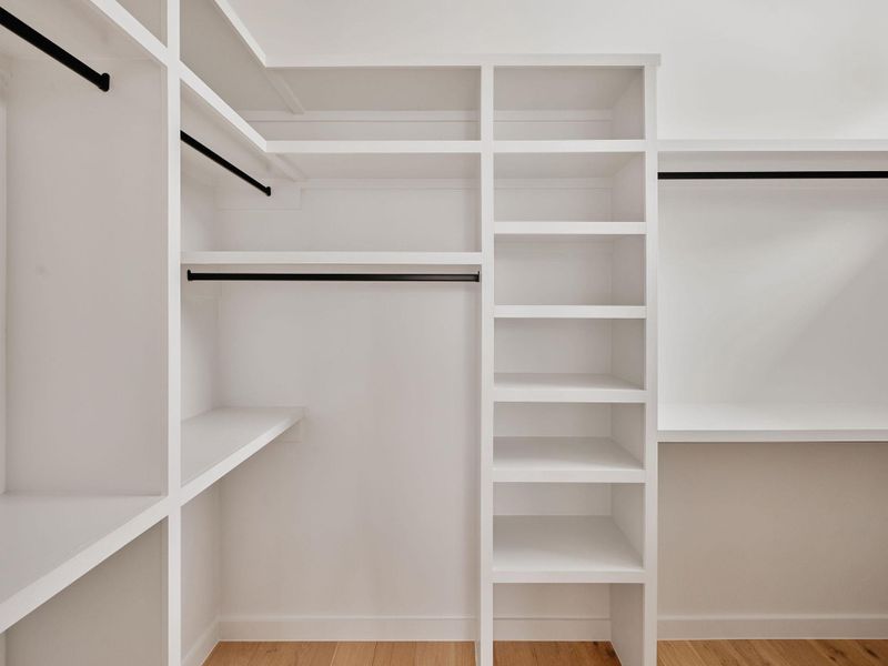Custom closet system featuring white shelving units, multiple hanging rods in a matte black finish, integrated cubbies, and wood-finish flooring