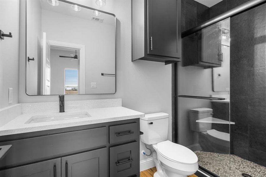 Bathroom featuring ceiling fan, vanity, an enclosed shower, and toilet