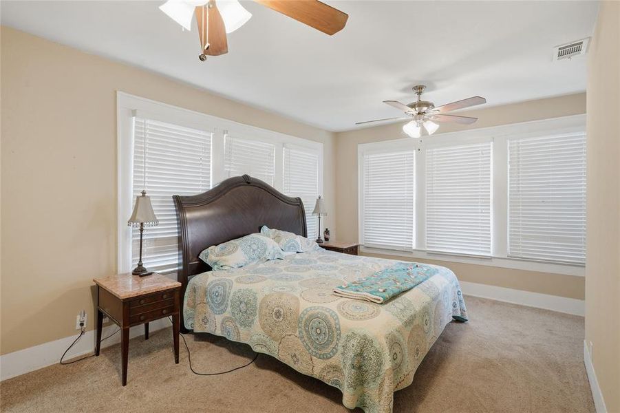 Bedroom featuring three large windows with blinds, neutral-toned walls, and a ceiling fan with integrated lighting