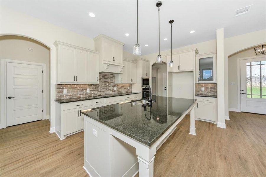 Kitchen featuring backsplash, light hardwood / wood-style floors, an island with sink, sink, and dark stone counters