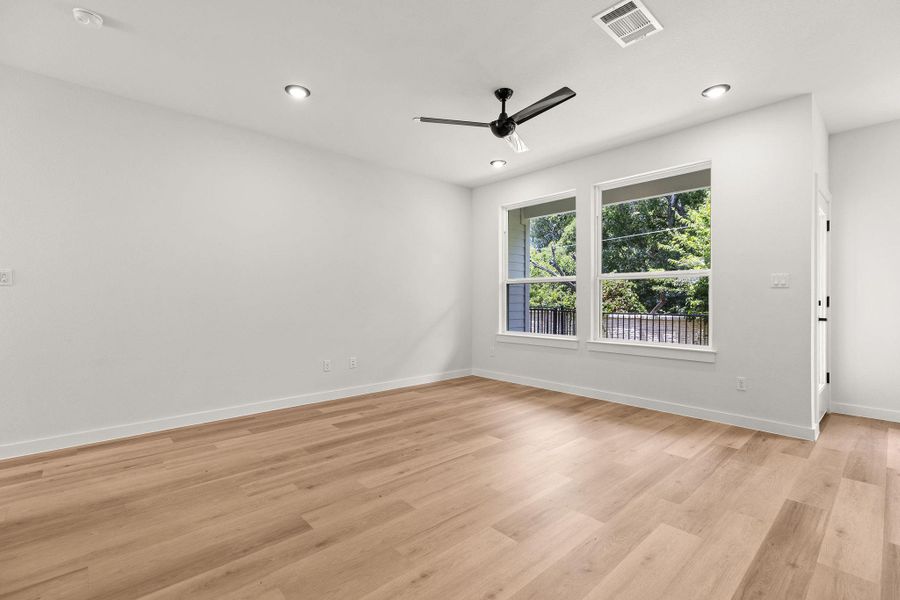 Well-lit living area featuring rich hardwood flooring and a stylish ceiling fan.