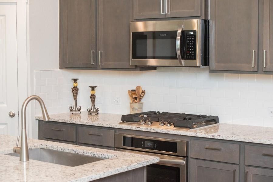 Kitchen featuring appliances with stainless steel finishes, backsplash, dark brown cabinets, and light stone countertops