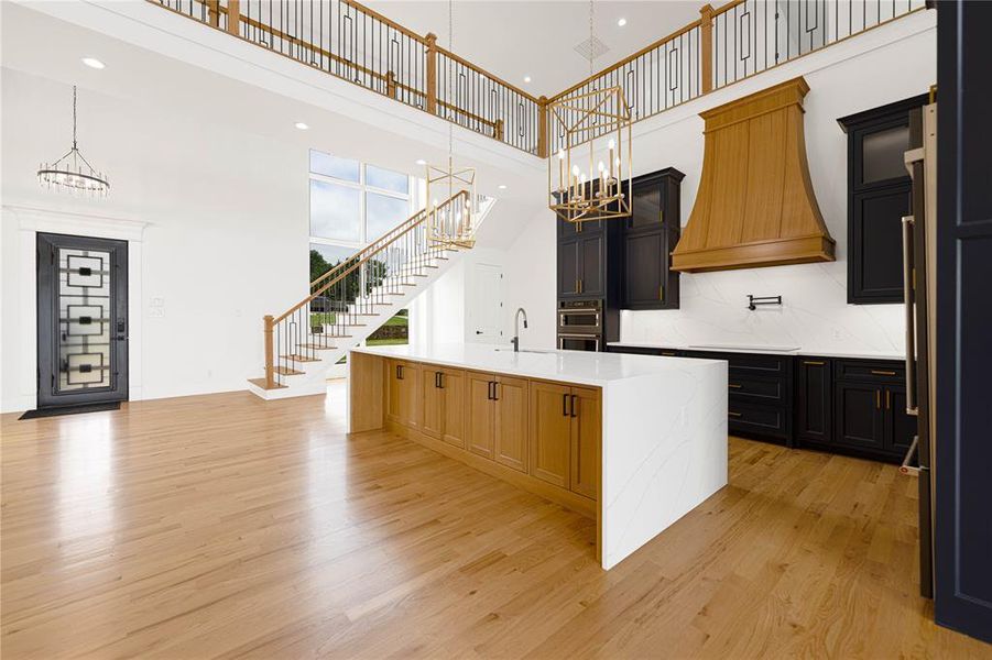 Dual tone kitchen featuring suspended lighting, light stone counters, a spacious island, light wood-type flooring, and black appliances
