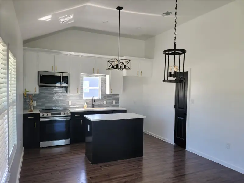 Kitchen featuring stainless steel appliances, two tone color scheme, a kitchen island, backsplash, and dark wood-style flooring