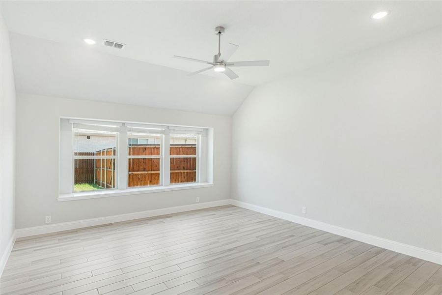 Empty room with vaulted ceiling, ceiling fan, light wood floors, and large triple window