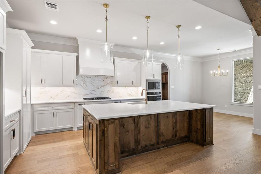 Two tone kitchen featuring tasteful backsplash, a center island with sink, light wood-type flooring, dual tone cabinets, and ornamental molding