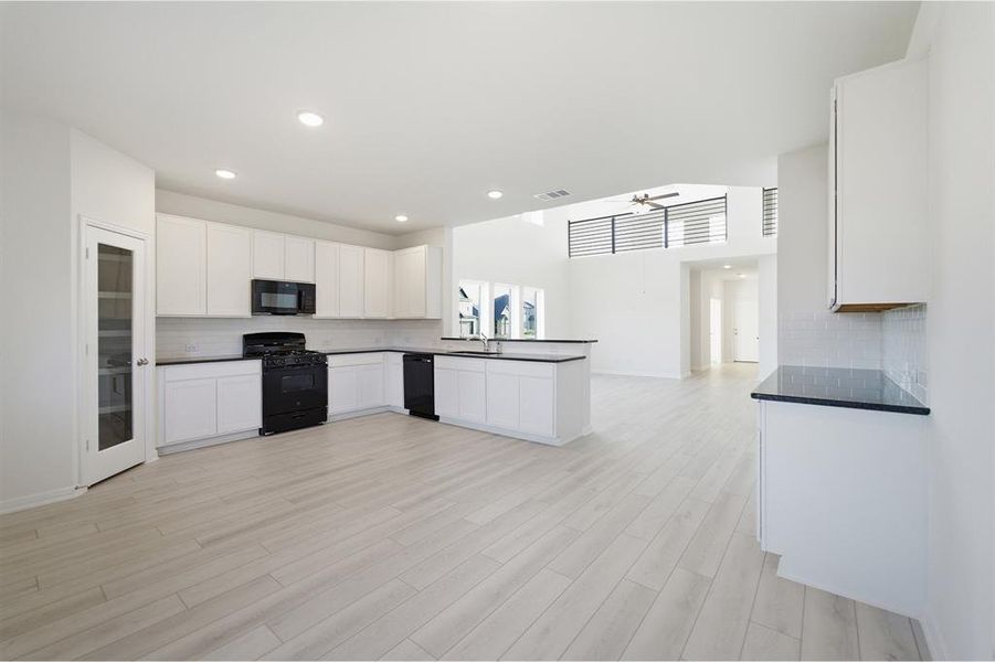 Open-concept kitchen featuring white cabinetry, dark countertops, black appliances, white subway tile backsplash, and light wood-finish flooring