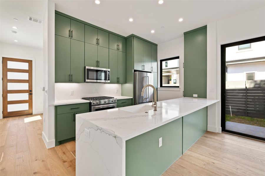 Kitchen featuring green cabinets, stainless steel appliances, a peninsula, light wood-style flooring, and recessed lighting