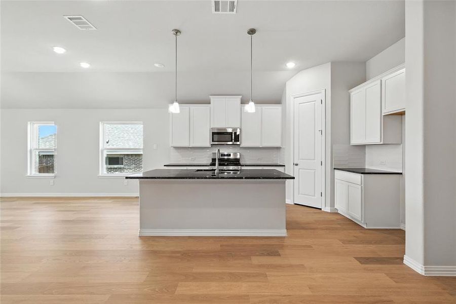 Kitchen with an island with sink, light wood-type flooring, white cabinetry, stainless steel appliances, and lofted ceiling