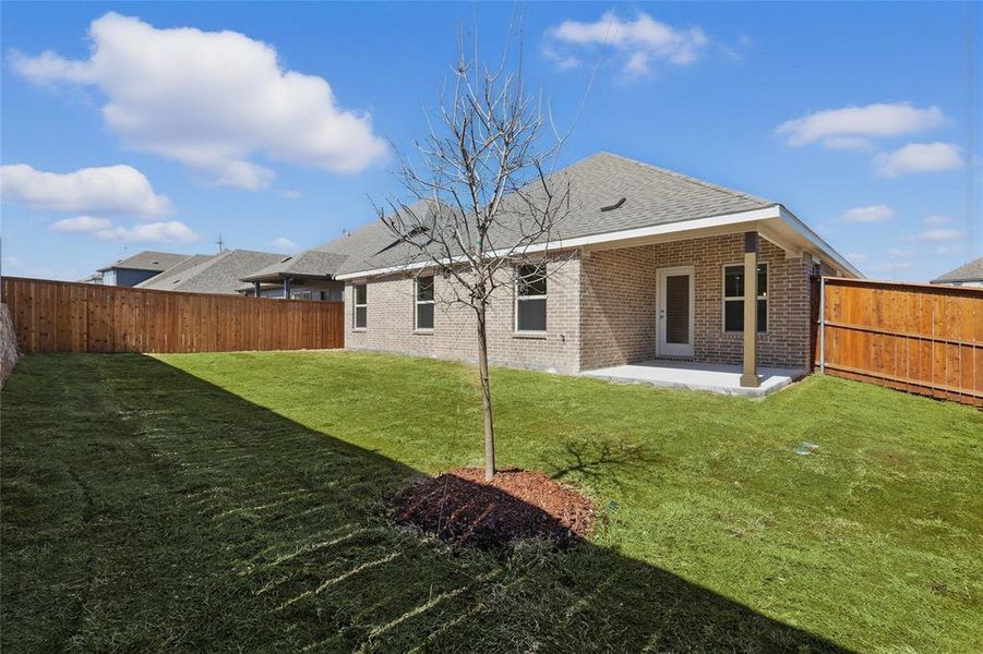 Back of house with brick siding, a fenced backyard, a lawn, and a patio