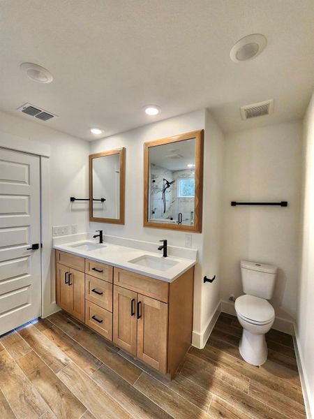 Bathroom featuring double vanity, a marble finish shower, wood finish floors, and recessed lighting