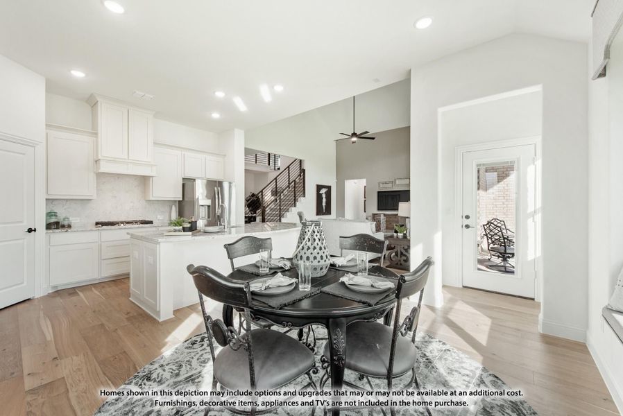 Open dining area with round dark table, hardwood floors, and white kitchen visible in background