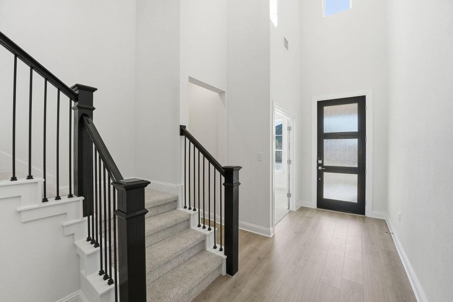 Entryway with stairway, light wood finished floors, and a towering ceiling