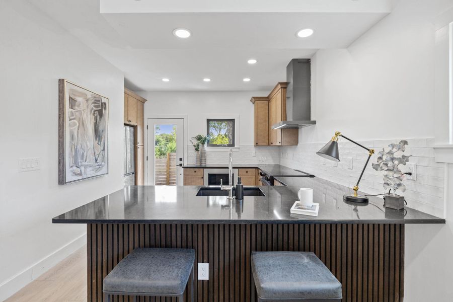 Kitchen with backsplash, recessed lighting, a kitchen breakfast bar, wall chimney exhaust hood, and a peninsula