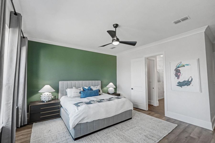 Spacious bedroom with accent wall, ceiling fan, and large window for natural light. Opens to an en-suite bath and features ample space for furnishings.