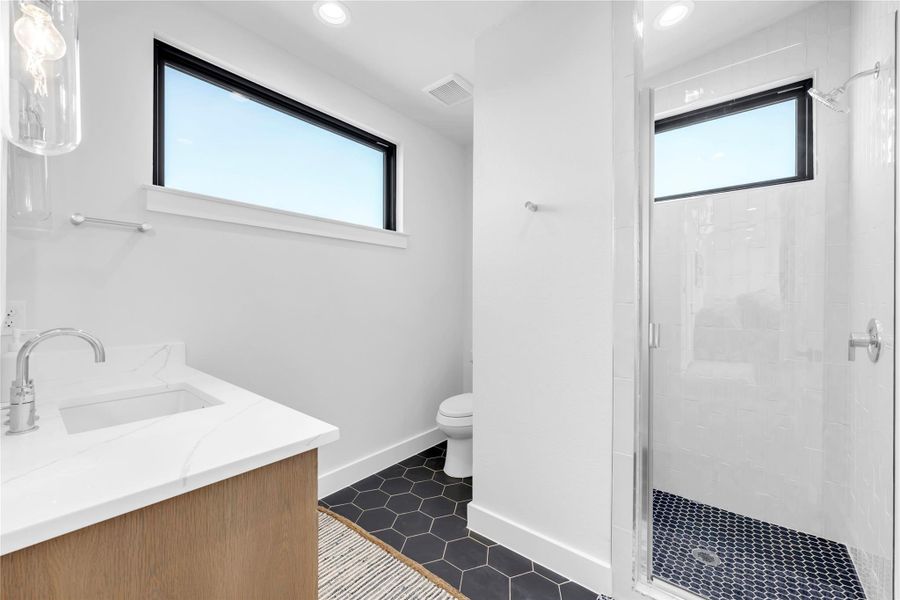 Bathroom seven: A modern bathroom features a glass-enclosed shower, stone-look vanity, and sleek dark hexagonal tile flooring.