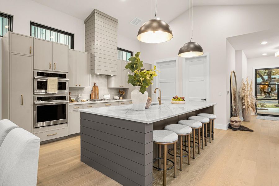Kitchen featuring light wood-style floors, light stone countertops, high vaulted ceiling, a breakfast bar area, and decorative backsplash