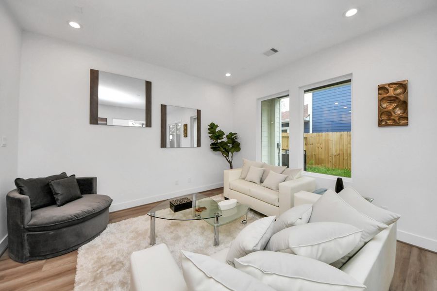 This inviting living room boasts a modern, airy design with sleek white walls, plush seating, a stylish glass coffee table, and abundant natural light streaming through large windows, offering a perfect blend of comfort and elegance.