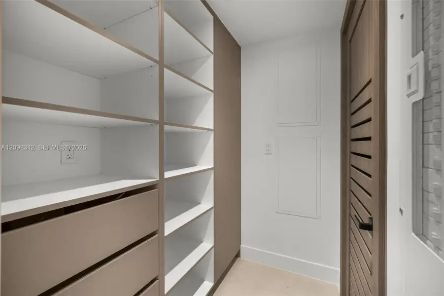 Custom built-in storage unit featuring adjustable shelving, integrated soft-close drawers, and a neutral wood-finish frame, complemented by a louvered-style door Custom built-in storage unit featuring adjustable shelving, integrated soft-close drawers, and a neutral wood-finish frame, complemented by a louvered-style door