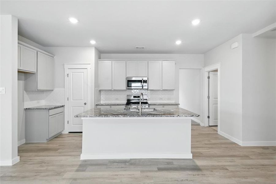 Kitchen with stone counters, decorative backsplash, an island with sink, appliances with stainless steel finishes, and recessed lighting
