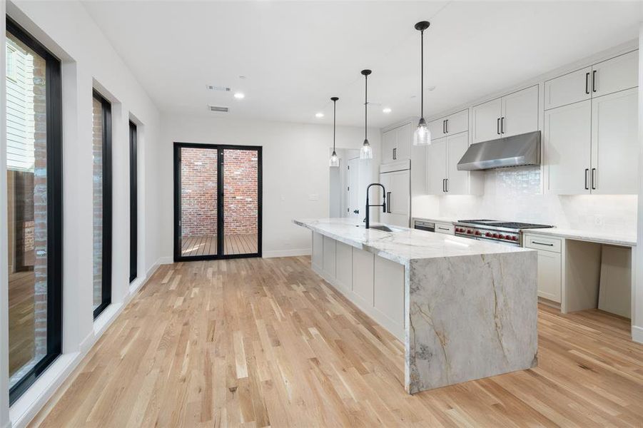 Kitchen with a kitchen island with sink, light stone counters, light hardwood / wood-style floors, decorative backsplash, and white cabinets